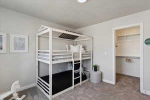 Bedroom featuring light gray walls, plush gray carpet, and a built-in closet with shelving and hanging rods