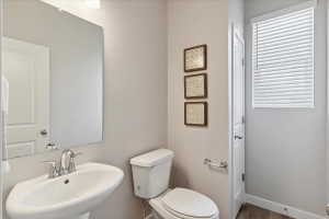 Powder room featuring a pedestal sink with chrome faucet, a rectangular wall-mounted mirror, a two-piece toilet, and wood-finish flooring