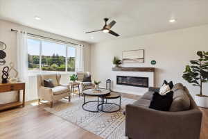 Spacious living area featuring large windows, wood-finish flooring, a modern linear fireplace with a distressed wood mantel, recessed lighting, and a ceiling fan