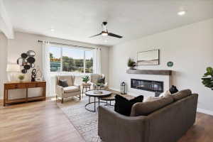 Spacious living area featuring wood-finish flooring, a modern linear fireplace with a wood mantle, a ceiling fan, and recessed lighting