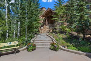 Stone facade home with a covered entry featuring exposed timber beams, a stone pathway, and mature trees