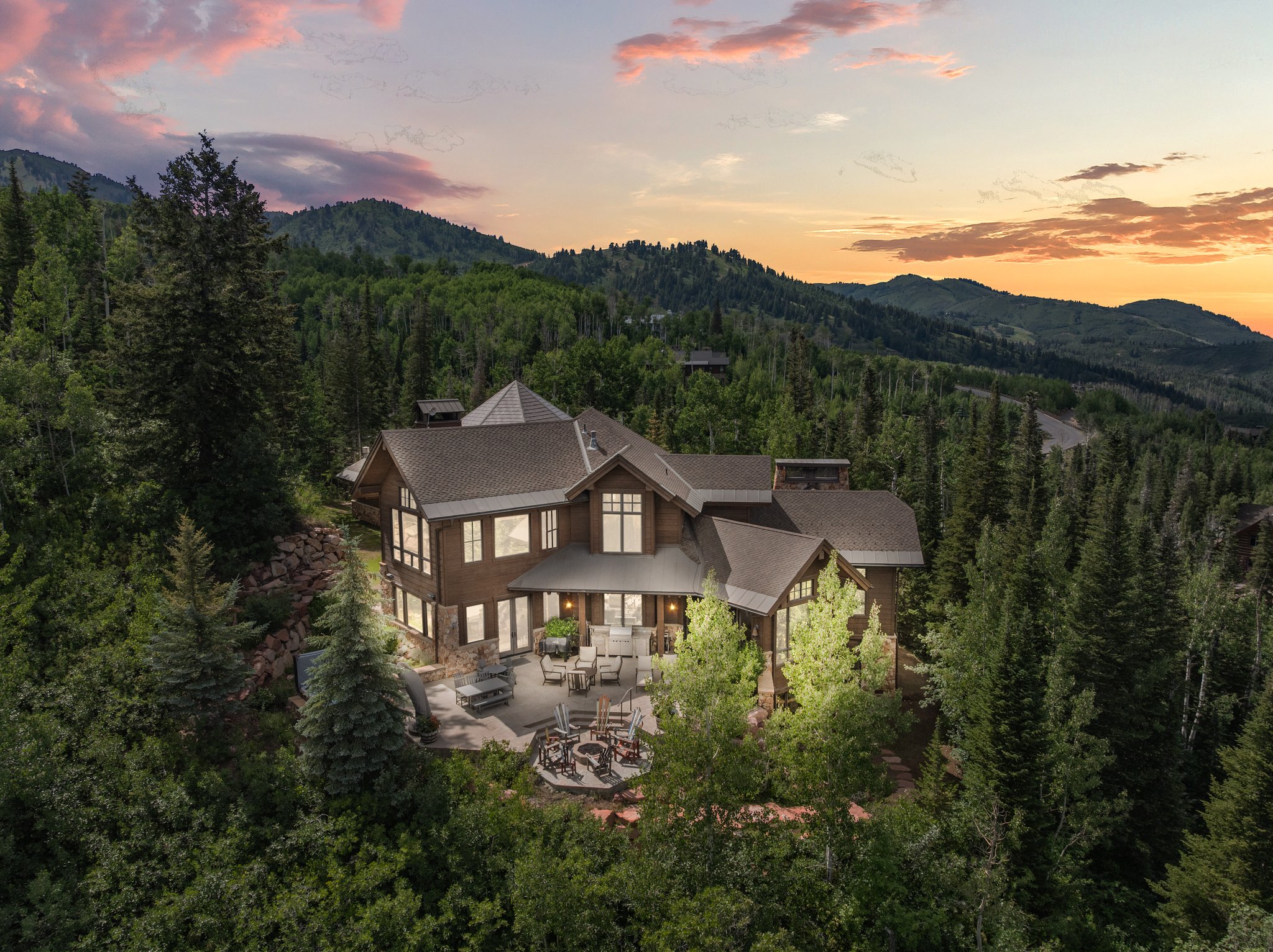 Expansive hillside residence featuring a multi-level stone patio, outdoor fire pit, and mature tree landscaping