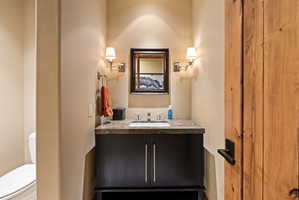 Powder room featuring a dark wood vanity with a stone-finish countertop and integrated sink, framed mirror, and wall sconces