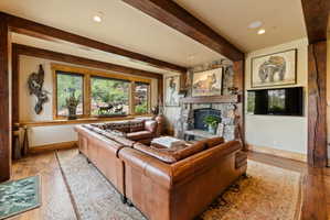 Spacious living area featuring exposed wood beams, a stone fireplace, wood-finish flooring, and a large window overlooking natural scenery