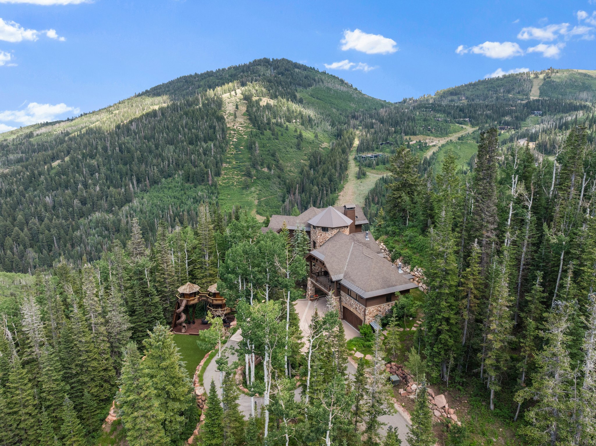 Mountain-side residence featuring extensive natural stone and wood siding, a multi-car garage, and a winding paved driveway