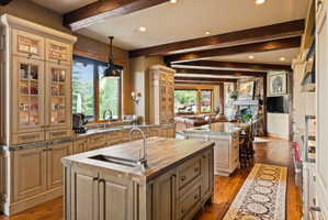 Gourmet kitchen with two islands, light-toned cabinetry with glass-front uppers, wood-finish flooring, and exposed ceiling beams