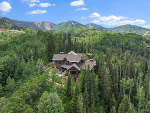 Expansive mountain-side property featuring a multi-level residence with stone and wood siding, surrounded by mature evergreen and deciduous trees
