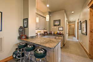 Built-in wet bar featuring a stone countertop, light wood-finish cabinetry, and pendant lighting