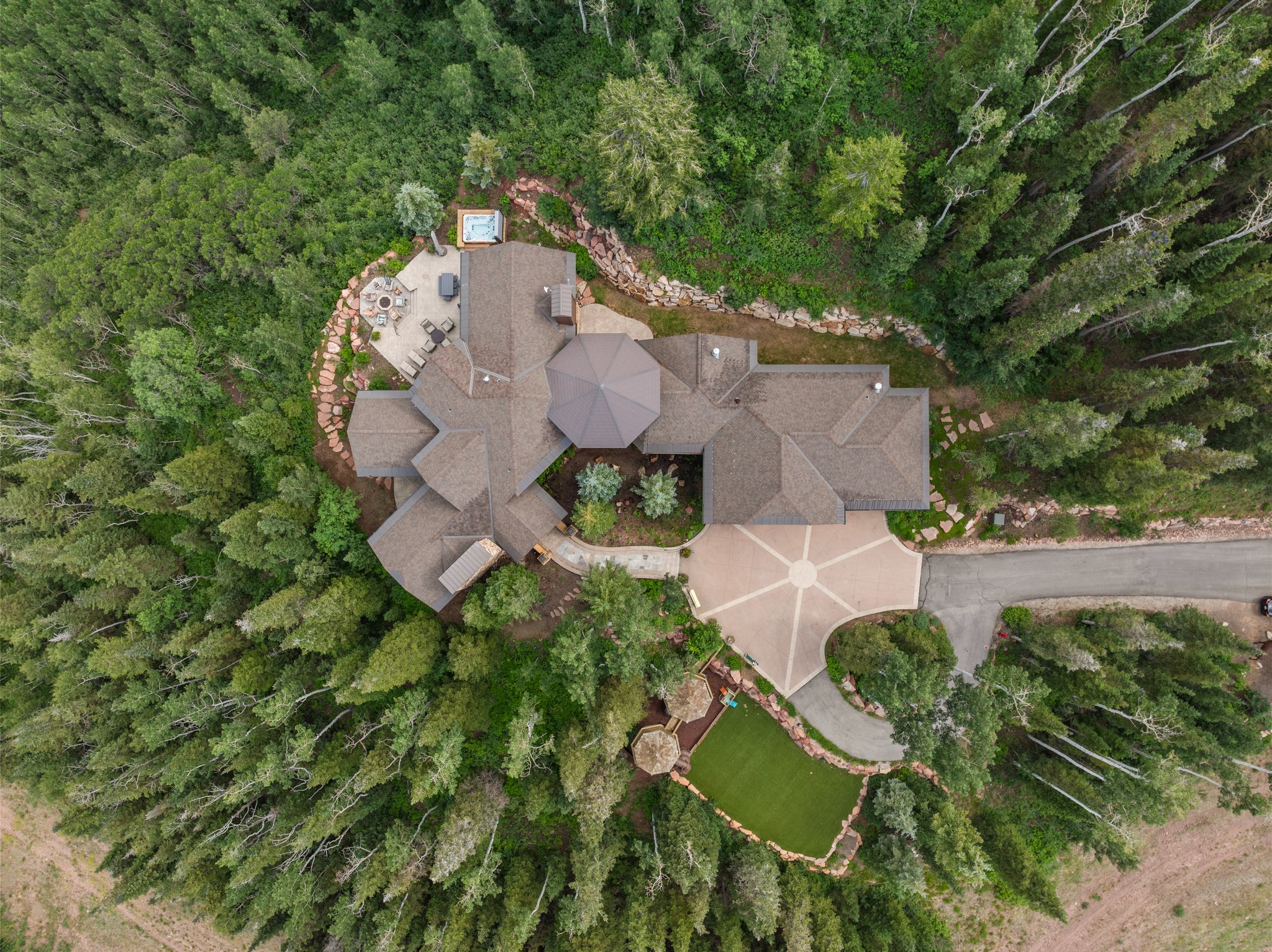 Expansive property featuring a multi-gabled roofline, a large paved driveway with a central design element, a stone patio, and a built-in outdoor spa