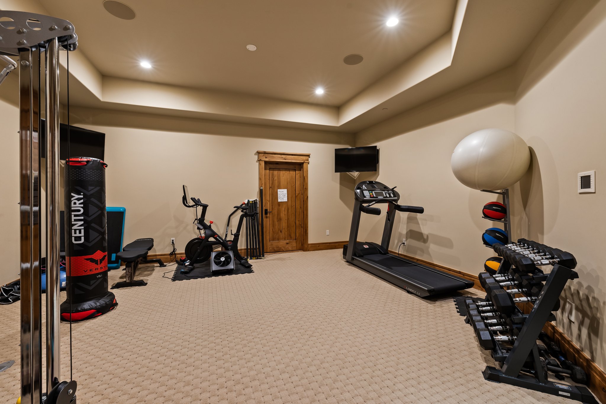 Dedicated fitness room featuring recessed lighting, tray ceiling details, textured carpet flooring, and a solid wood door