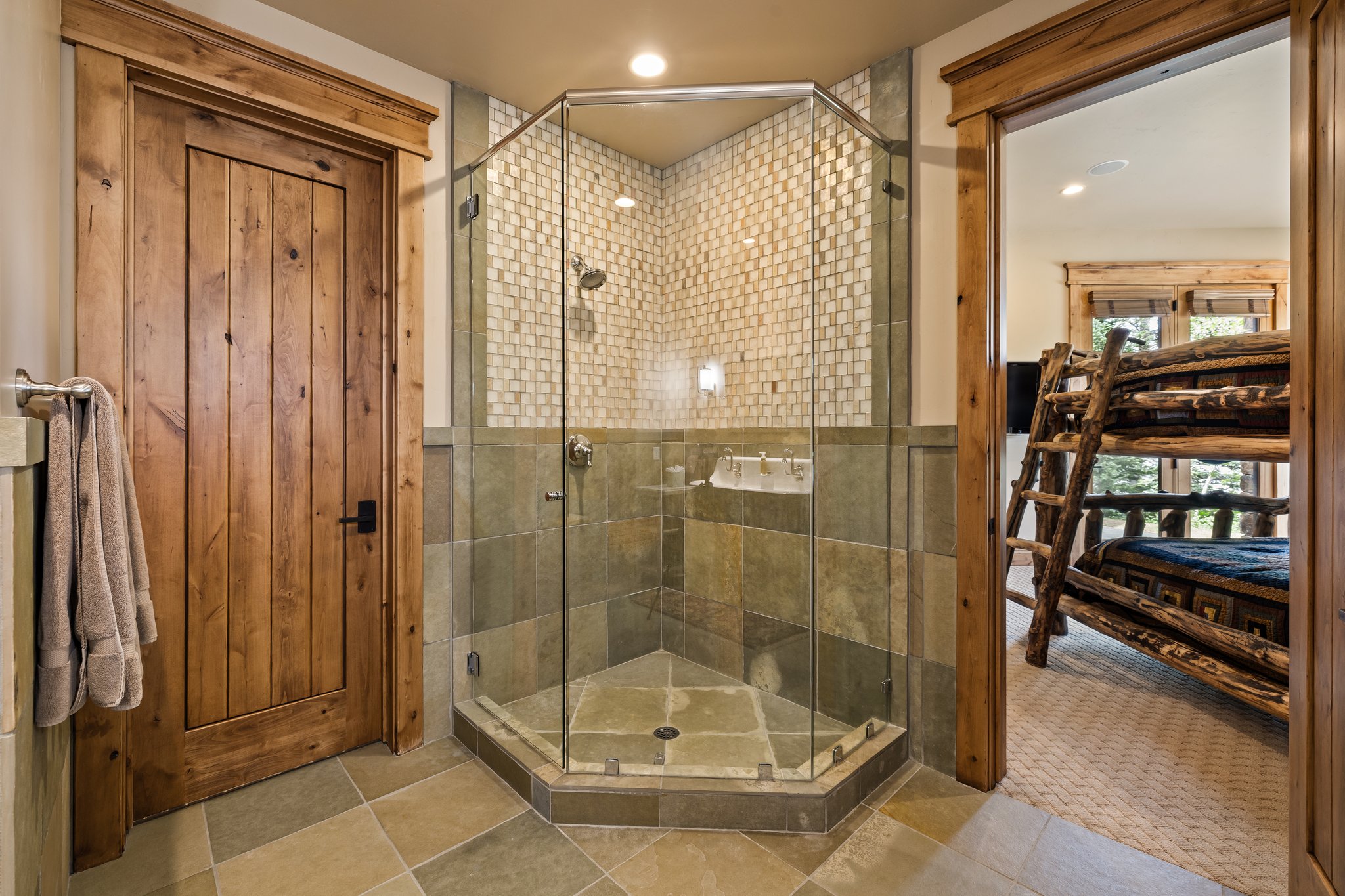 Corner glass shower enclosure with floor-to-ceiling tilework, including small square mosaic tile and large format stone tile