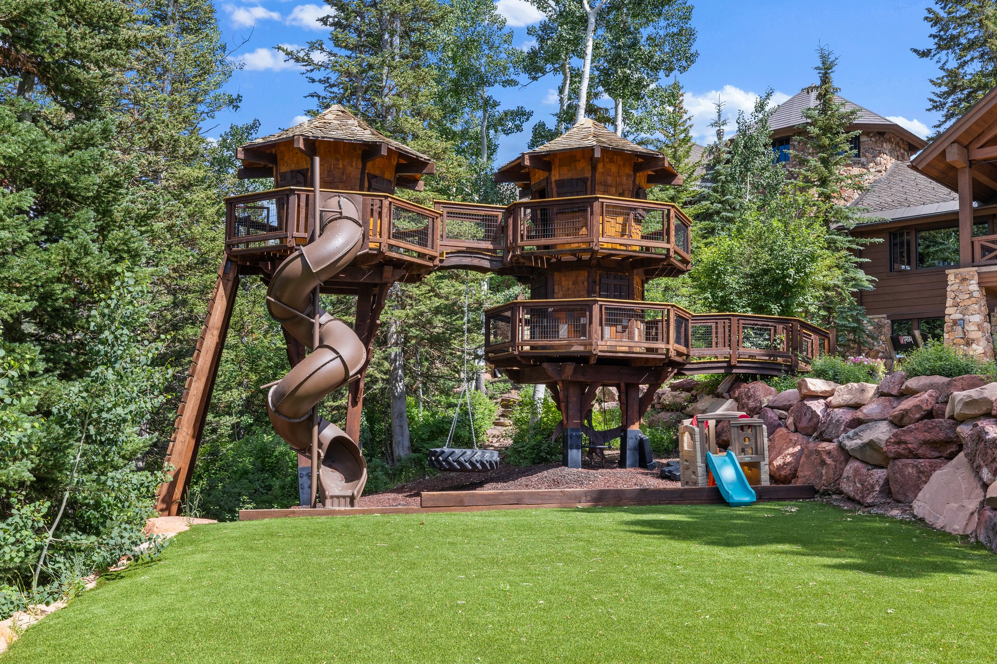 Custom treehouse structure featuring multiple levels, connecting walkways, and a spiral slide