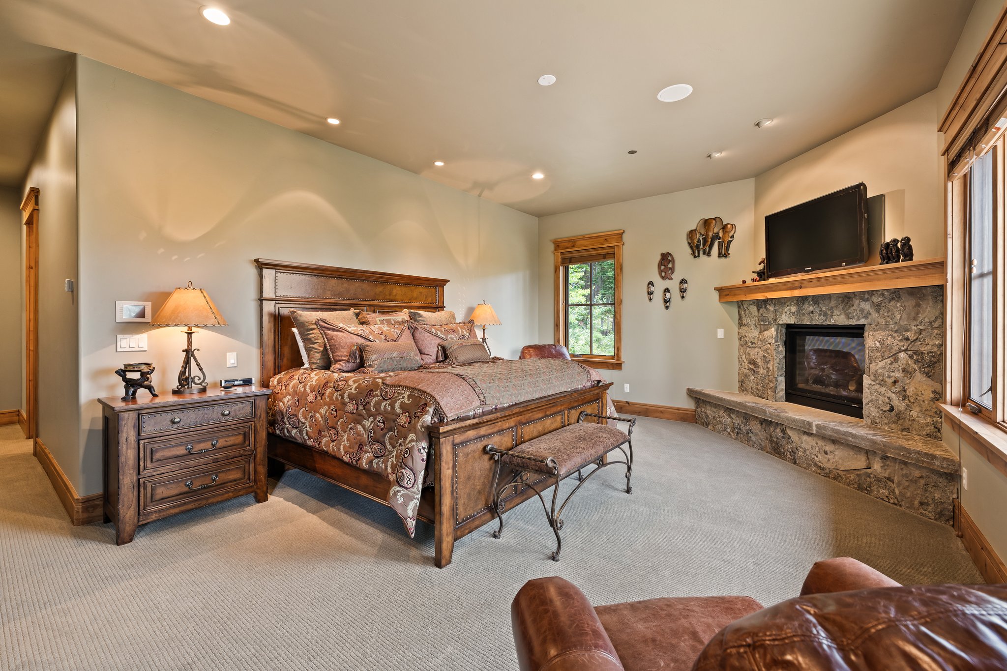 Carpeted room featuring a stone fireplace with a wood mantle, recessed lighting, and multiple windows with wood trim