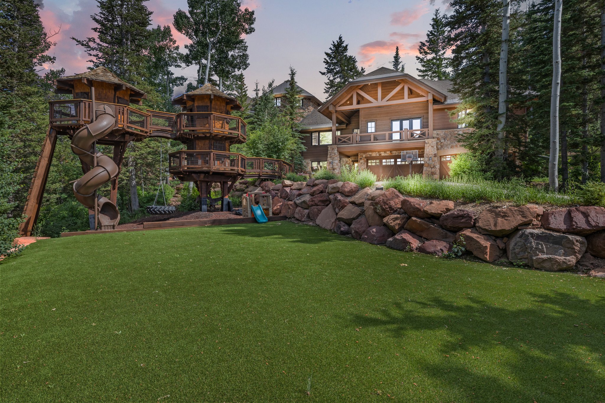 Expansive synthetic turf lawn with a multi-level wooden play structure featuring slides and elevated platforms