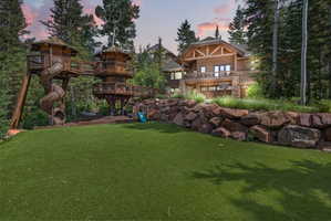 Expansive synthetic turf lawn with a multi-level wooden play structure featuring slides and elevated platforms