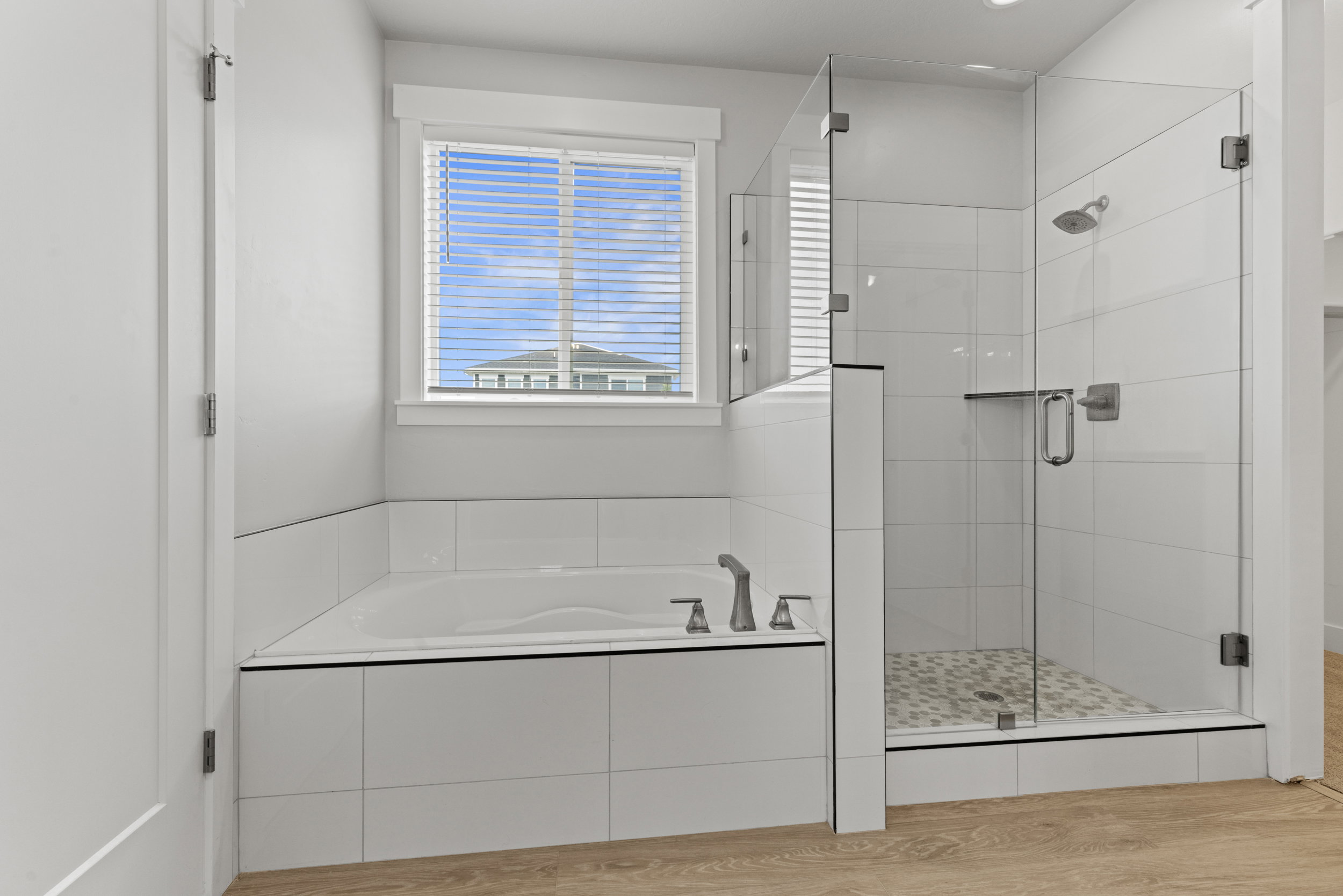 Contemporary bathroom featuring an integrated soaking tub, an expansive glass-enclosed shower with a tiled floor, wood-finish flooring, and a window with blinds