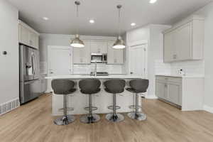 Kitchen featuring a central island with white countertop, pendant lighting, light wood-finish flooring, and light-toned cabinetry
