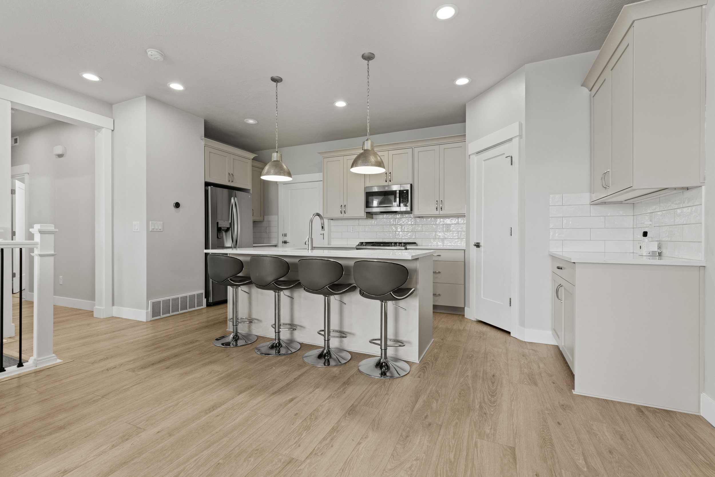 Open concept kitchen featuring an island with seating, pendant lighting, stainless steel appliances, light wood-finish flooring, and white subway tile backsplash
