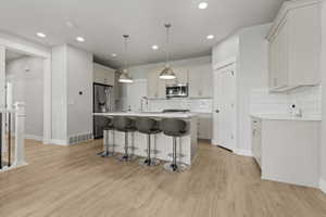 Open concept kitchen featuring an island with seating, pendant lighting, stainless steel appliances, light wood-finish flooring, and white subway tile backsplash