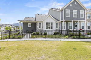 Contemporary townhome exterior featuring gray siding, white trim, stone accents, and a black metal fence with gate