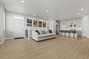 Open-concept living area featuring light wood-finish flooring, white cabinetry, and recessed lighting