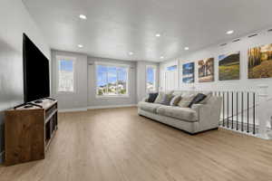 Bright living space featuring wood-finish flooring, recessed ceiling lighting, and a white staircase with black metal balusters