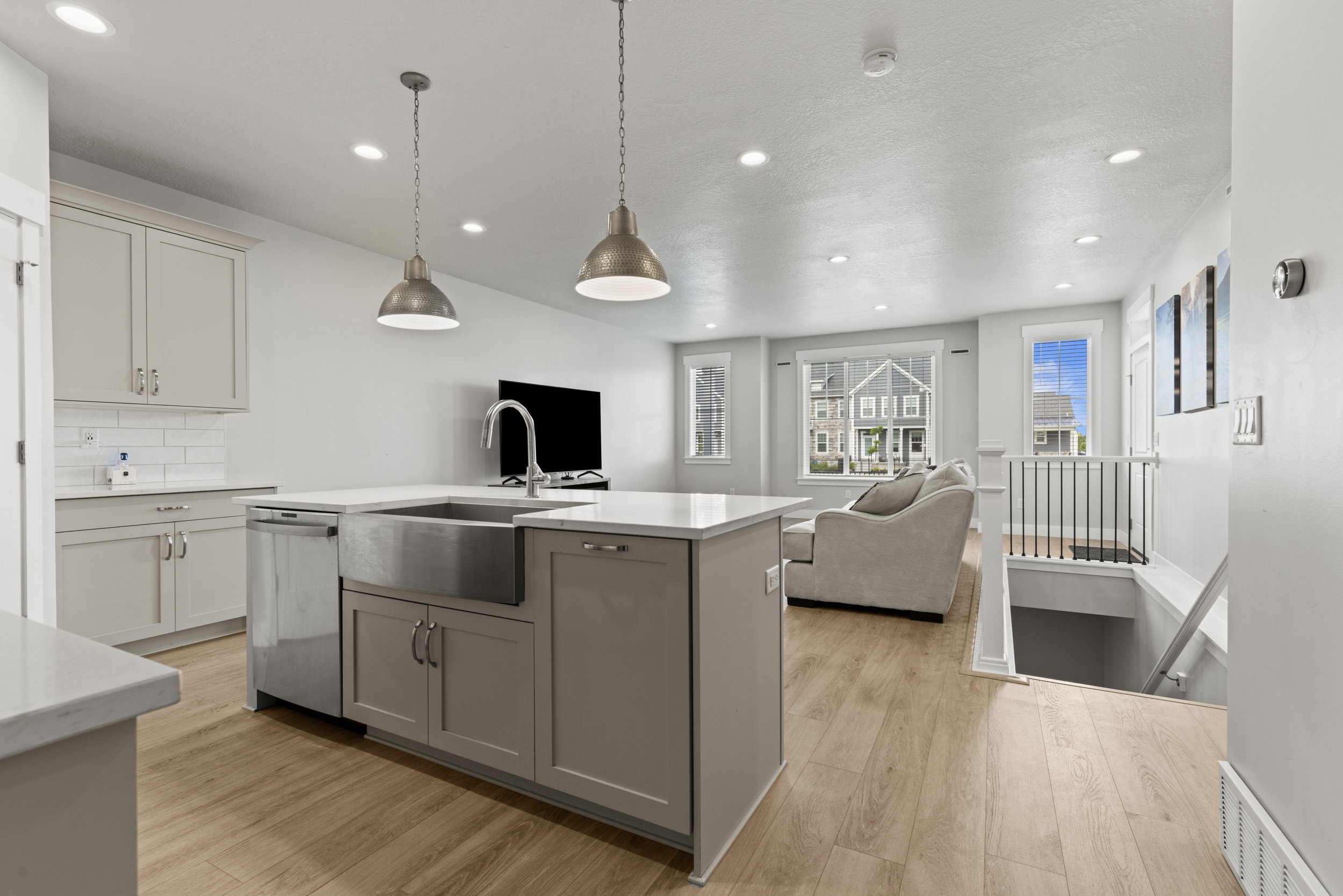Kitchen island featuring a stainless steel farmhouse sink, integrated dishwasher, and pendant lighting