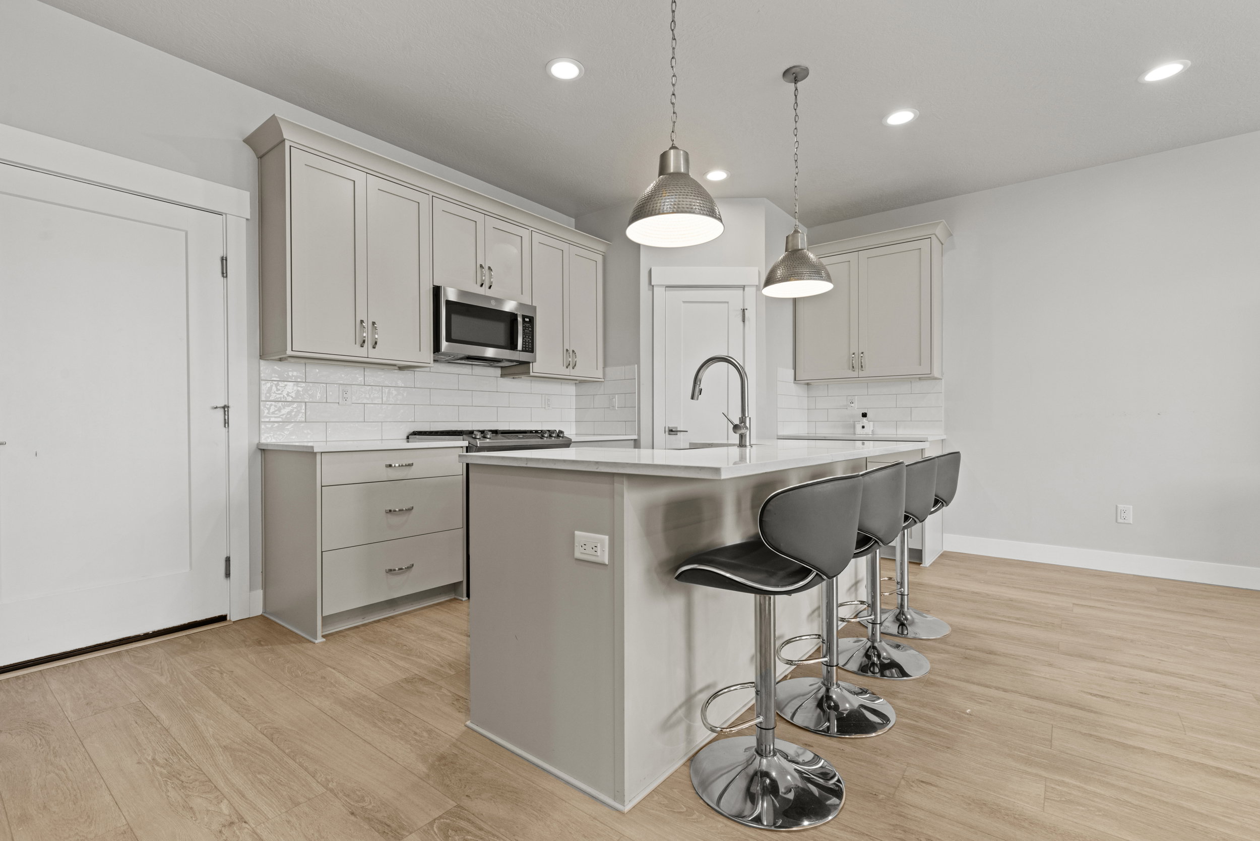Kitchen featuring light wood-finish flooring, white subway tile backsplash, stainless steel appliances, and an island with pendant lighting