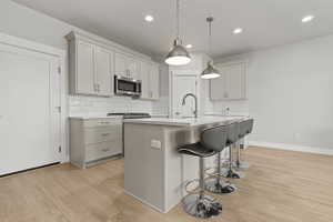 Kitchen featuring light wood-finish flooring, white subway tile backsplash, stainless steel appliances, and an island with pendant lighting