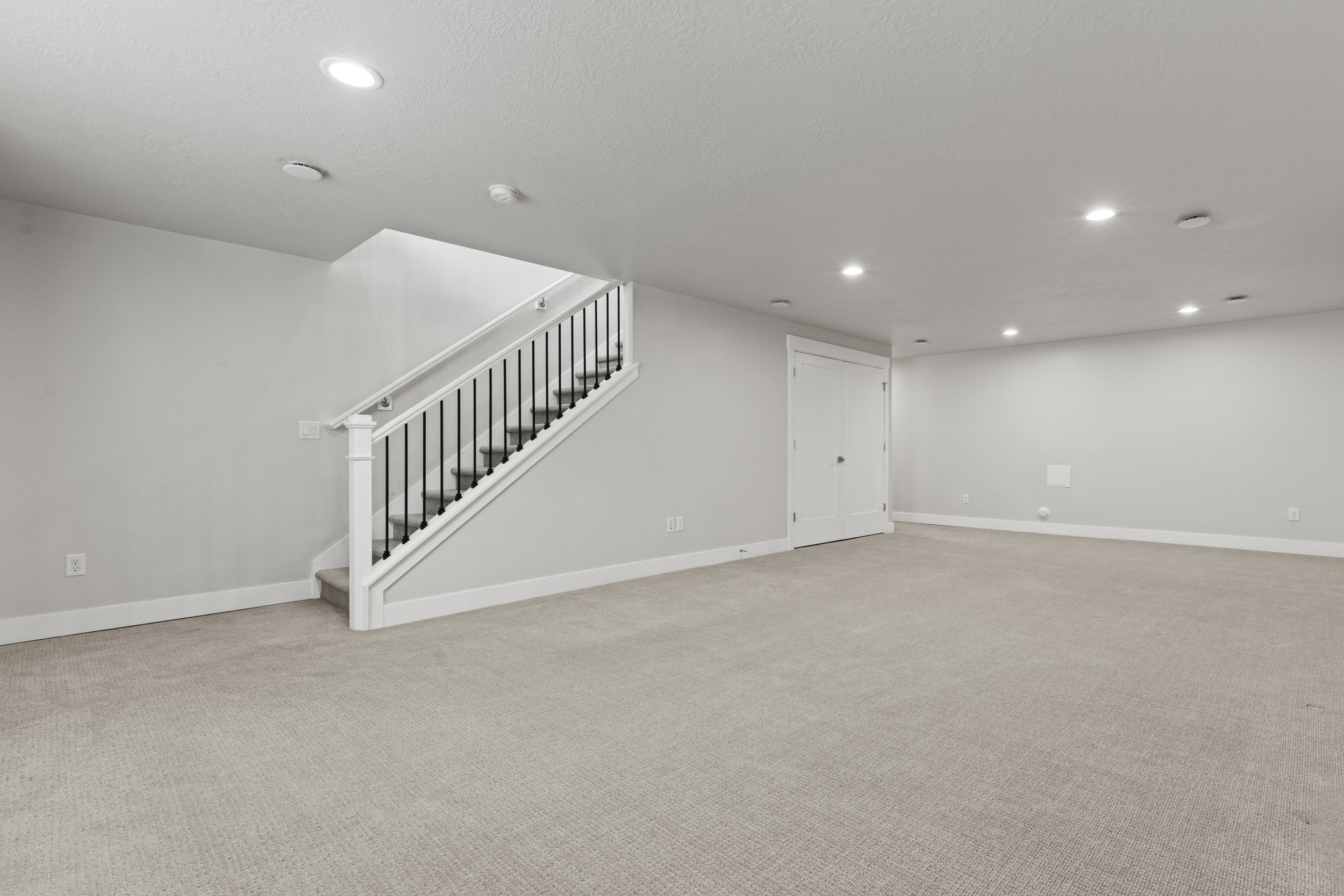 Spacious room featuring carpet flooring, recessed lighting, a staircase with white newel posts and black balusters, and a solid white door