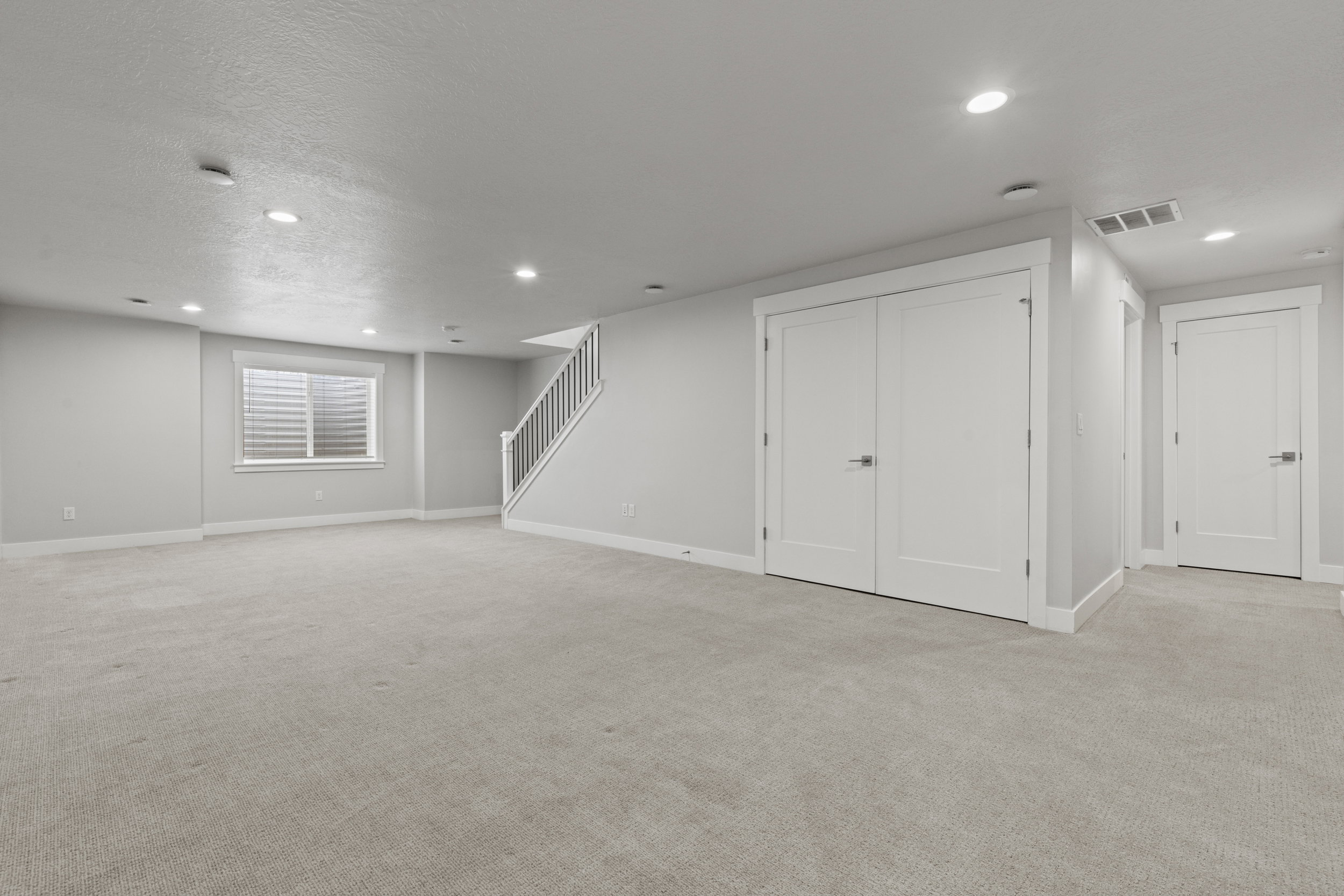 Spacious lower-level room featuring light gray carpeting, recessed lighting, and white trim