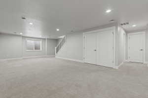 Spacious lower-level room featuring light gray carpeting, recessed lighting, and white trim