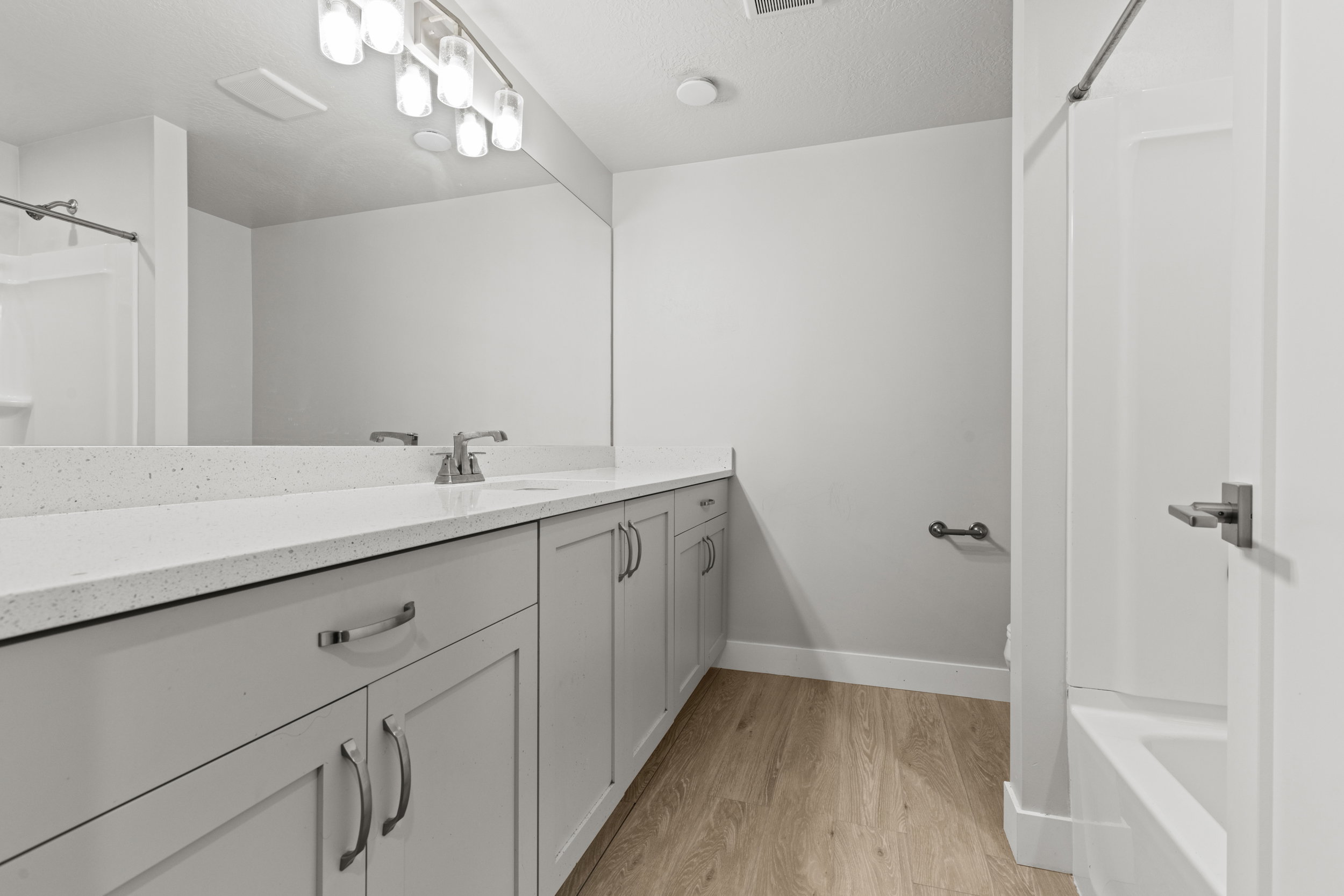 Bathroom featuring light gray shaker-style cabinetry with brushed nickel hardware, a white speckled countertop, and wood-finish flooring