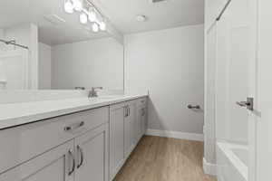 Bathroom featuring light gray shaker-style cabinetry with brushed nickel hardware, a white speckled countertop, and wood-finish flooring
