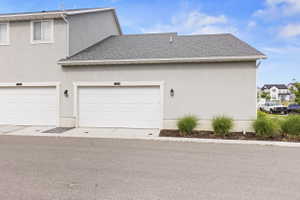 White garage door with textured panels, light stucco exterior, and a dark shingle roof