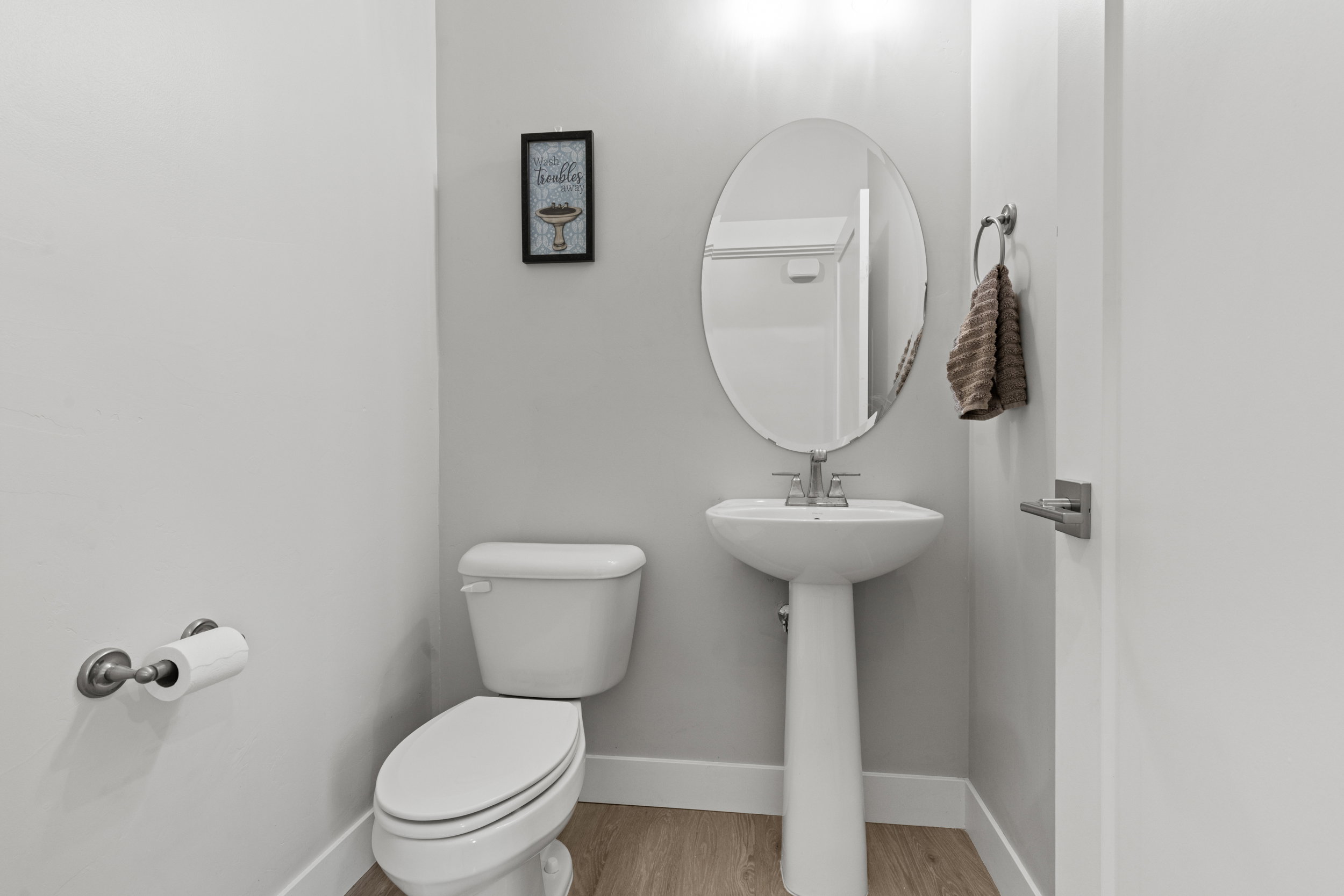 Pedestal sink with an oval mirror and brushed nickel fixtures