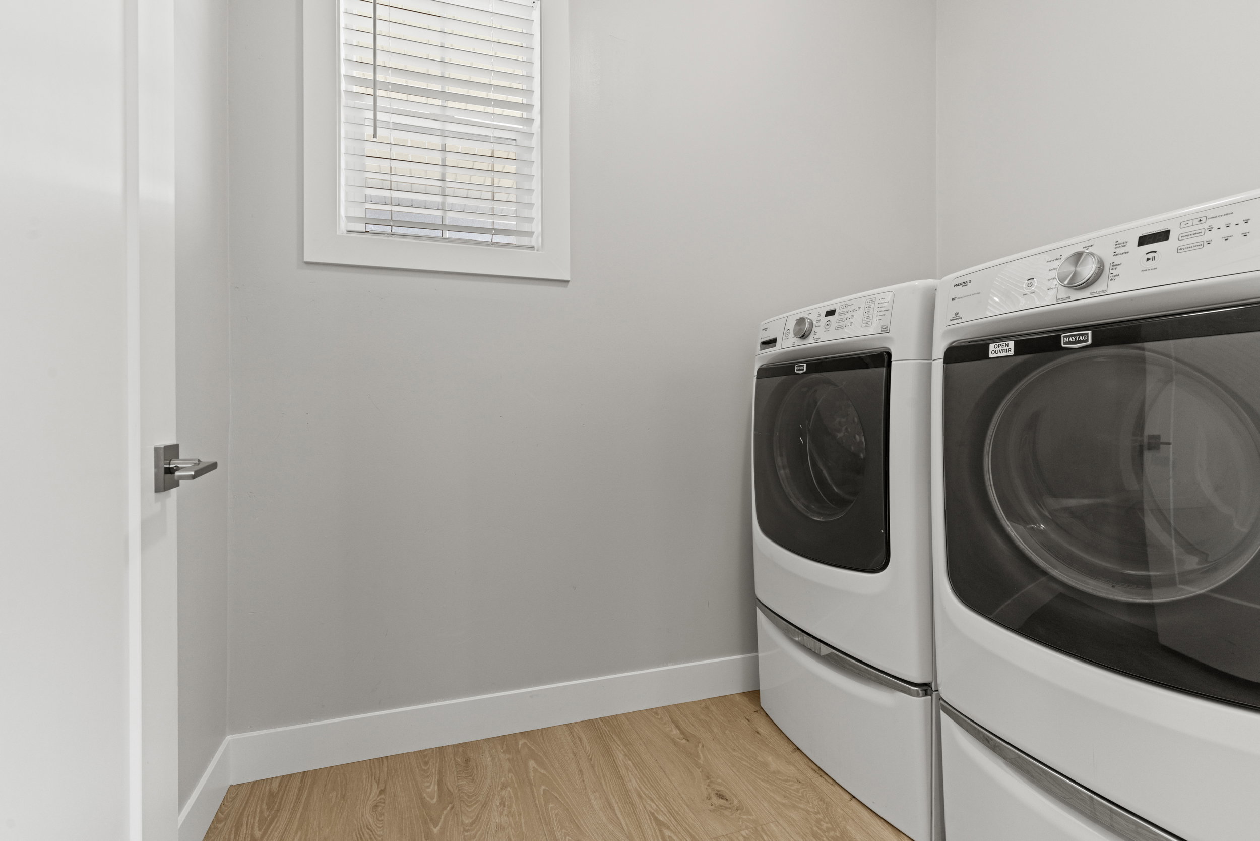 Dedicated laundry area featuring light wood-finish flooring, light gray wall paint, and white trim