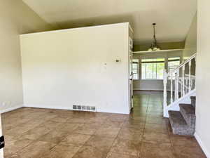 Spacious interior featuring tile flooring, vaulted ceilings, a carpeted staircase with a white baluster railing, and a dining area with a multi-pane bay window