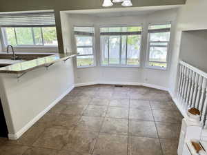 Bay window with multiple glass panes, ceramic tile flooring, a breakfast bar with a granite-style countertop, and a built-in kitchen sink