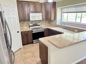 Kitchen featuring dark wood cabinetry, light speckled countertops, a tile backsplash, stainless steel range, and an undermount double sink with a gooseneck faucet