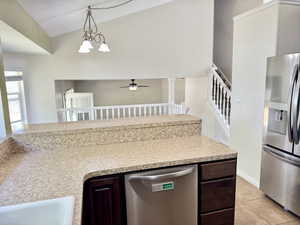 Kitchen counter with a built-in sink and stainless steel dishwasher, featuring dark wood-finish cabinetry, speckled countertops, and a stainless steel refrigerator