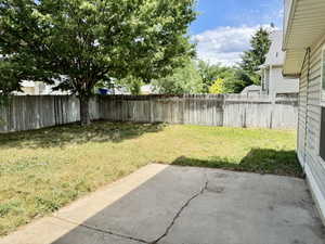 Spacious backyard featuring a concrete patio, mature shade tree, and wood privacy fencing