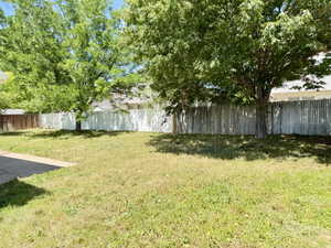 Expansive backyard featuring mature trees, a privacy fence, and a concrete patio section
