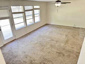 Spacious room featuring neutral carpeting, a ceiling fan with integrated lighting, multiple windows, and a glass-paneled door