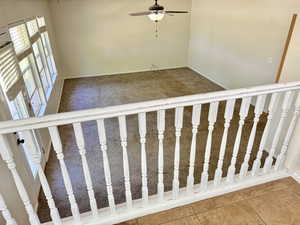Loft area overlooking a carpeted room featuring a ceiling fan with light, multiple windows, and white plantation shutters