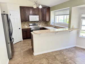 Kitchen featuring granite countertops, wood cabinetry, stainless steel appliances, a tiled backsplash, and tile flooring