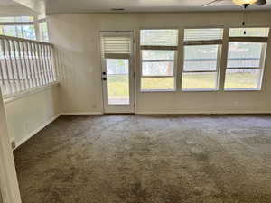 Living space featuring neutral carpeting, a white spindle railing, and a glass-paneled door opening to the exterior