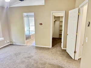 Carpeted room featuring a vaulted ceiling with a ceiling fan, an alcove with built-in shelving, a full bath with a tiled surround tub, and a window with horizontal blinds