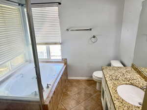 Bathroom featuring a built-in jetted tub, ceramic tile surround, and a vanity with a granite-style countertop and integrated sink