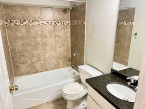 Bathroom featuring a white bathtub, ceramic tile shower surround with decorative mosaic accent, white toilet, and a vanity with a dark speckled countertop and integrated sink